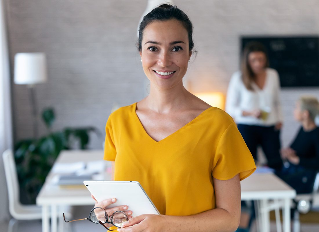 Business Insurance - Young Businesswoman Looking at Camera With Colleagues Working in the Office Background